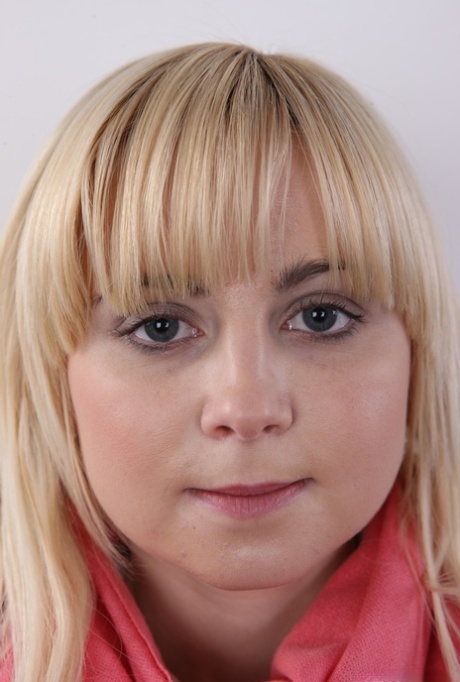 Plump blond girl removes her clothes until she's standing naked against a wall